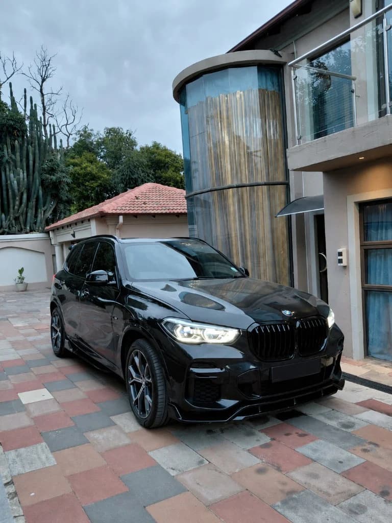 Black BMW X5 M Competition SUV with LED headlights on a stone-paved driveway